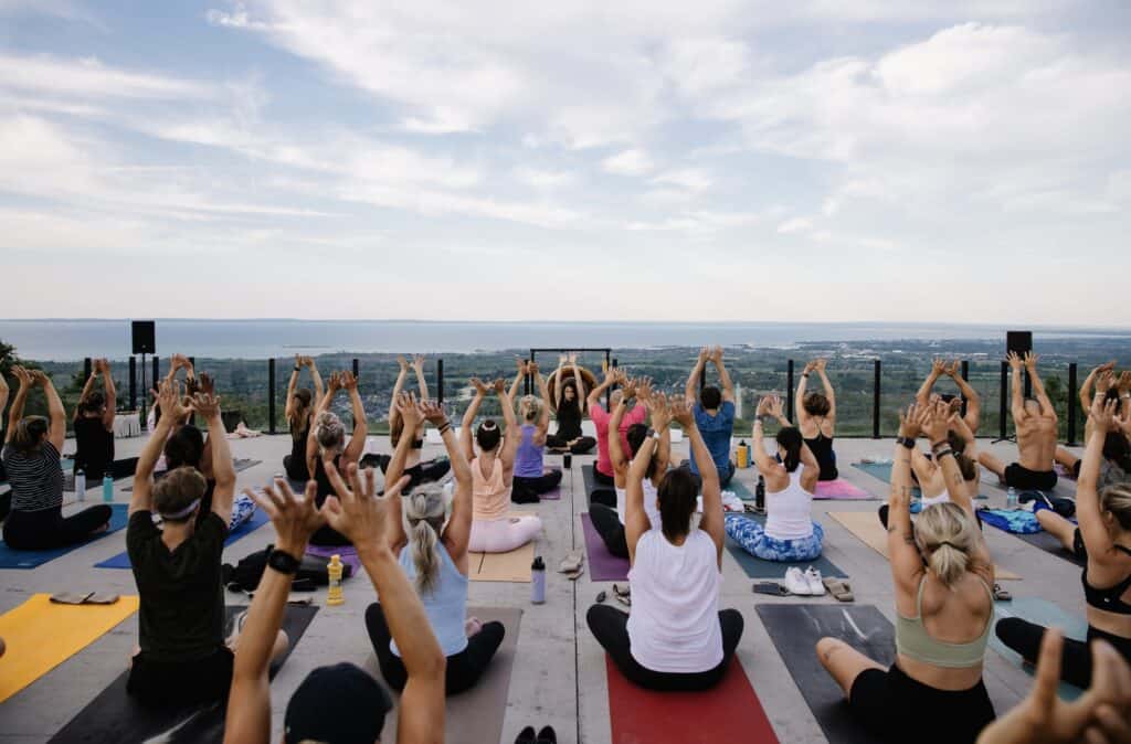Group of people practicing yoga on rooftop terrace with scenic city and ocean view.